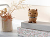 Wooden cat figurine on a stack of books with a vase of dried flowers in the background
