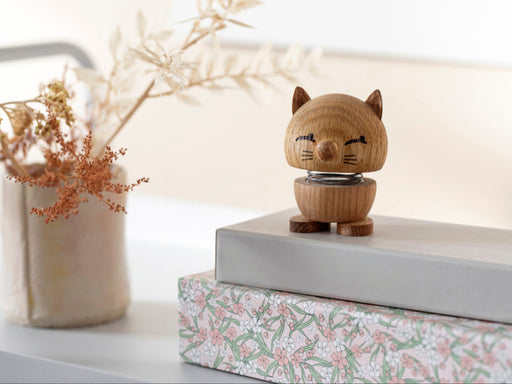 Wooden cat figurine on a stack of books with a vase of dried flowers in the background